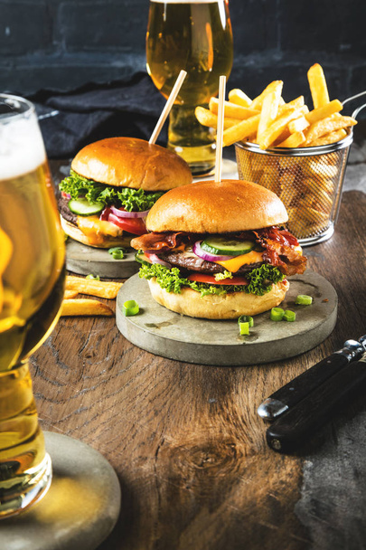 close-up view of glasses of beer, fresh tasty burgers and french fries on table - Foto, imagen
