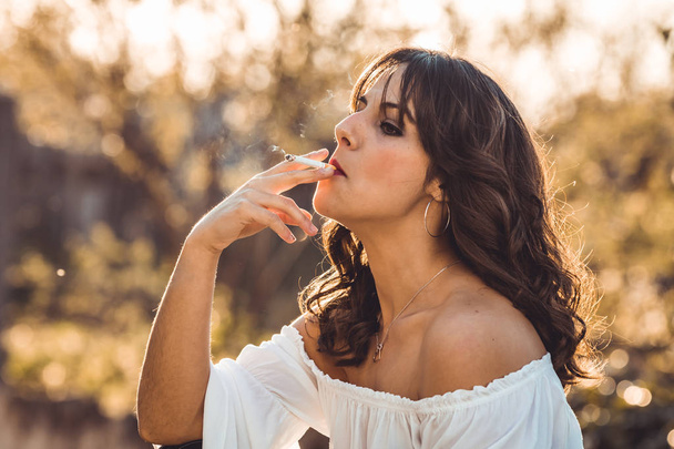 Young woman smoking outdoor at sunset - Фото, зображення
