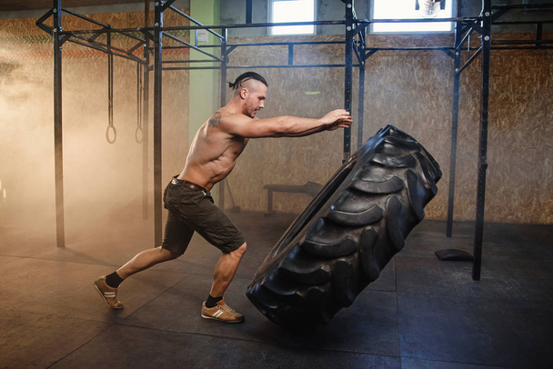 Young strong man flipping tire in the gym. - Фото, зображення