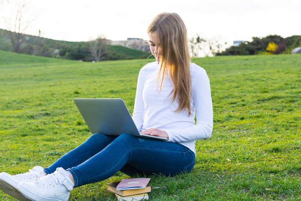 Joven hermosa estudiante con una computadora portátil y libros sentados en un
 - Foto, imagen