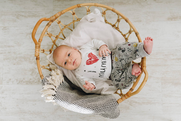 Um bebê bonito caucasiano top-down vestindo pijama cinza deitado em uma grande cesta no chão
  - Foto, Imagem