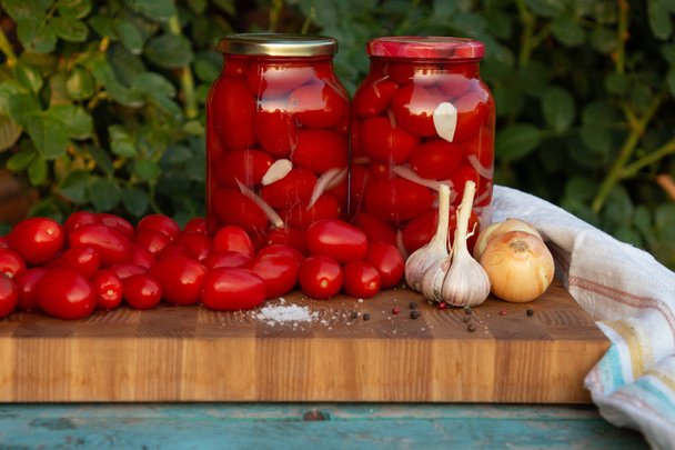 Маринованные помидоры с чесноком, луком и специями в стеклянных банках. Свежие помидоры на деревянном столе
. - Фото, изображение