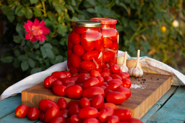 eingelegte Tomaten mit Knoblauch, Zwiebeln und Gewürzen in Glasgläsern. frische Tomaten auf einem Holztisch. - Foto, Bild