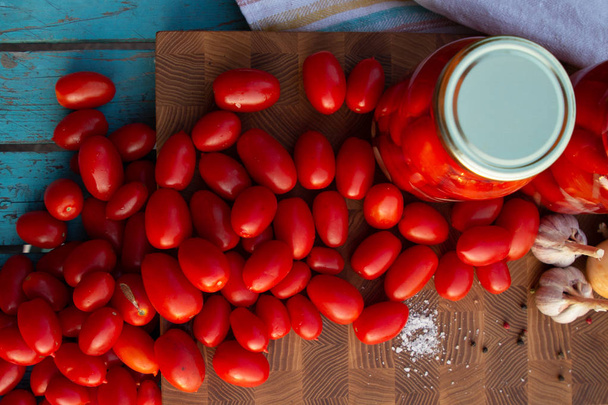 Marynowane pomidory z czosnkiem, cebulą i przyprawami w szklanych słoikach. Świeże pomidory na drewnianym stole. - Zdjęcie, obraz