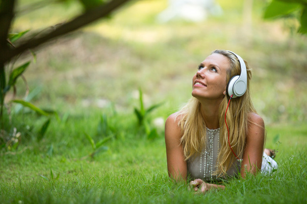 Beautiful emotional girl with headphones in the park at sunny day. - Photo, Image