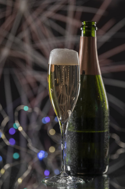 Una elegante copa con champán amarillo y espumoso y una elegante botella verde detrás. Concepto de celebración navideña. Imagen vertical
 - Foto, imagen