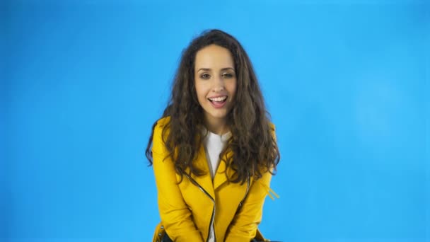 Sarı ceketli Mutlu Güzel Kadın Stüdyoda Göz Kırpan Mavi Arkaplan. - Video, Çekim