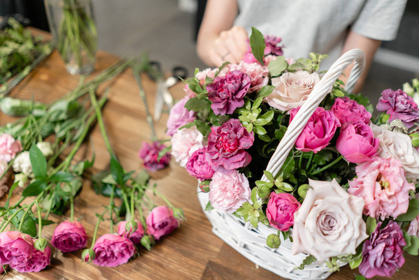 Mulher florista criar arranjo de flores em uma cesta de vime. Belo buquê de flores mistas. Conceito de loja floral. Bonito buquê fresco. Entrega de flores
 - Foto, Imagem