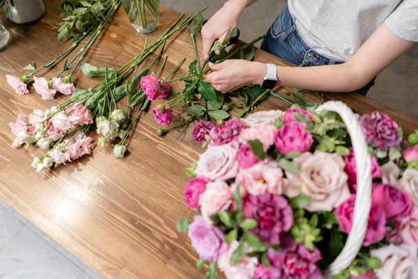 Kwiaciarnia kobieta stworzyć układ kwiatów w wiklinowym koszyku. Piękny bukiet mieszanych kwiatów. Koncepcja kwiaciarni. Przystojny świeży bukiet. Dostawa kwiatów - Zdjęcie, obraz