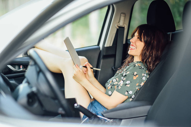 Žena píše v poznámkovém bloku s perem v bílém autě - Fotografie, Obrázek