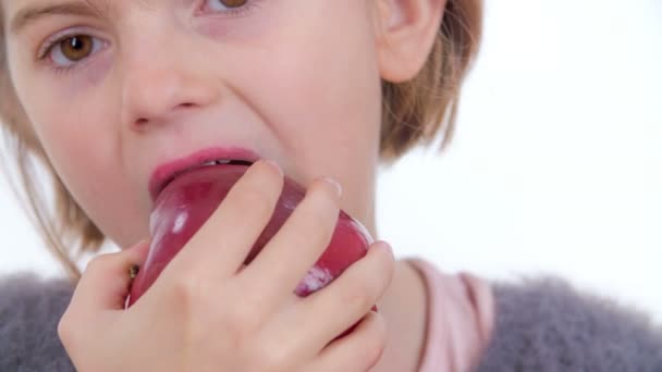 Ένα νεαρό κορίτσι τρώει ένα μικρό κόκκινο βιολογικό μήλο.. - Πλάνα, βίντεο