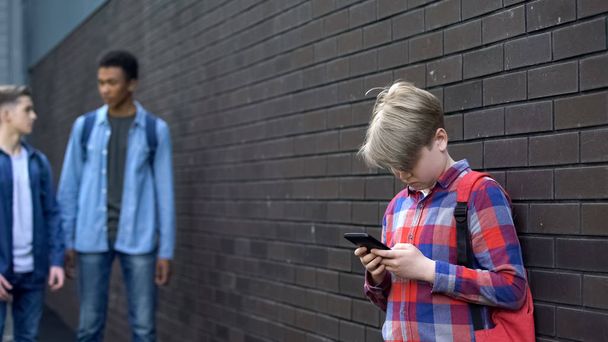 Junior student using cell phone standing lonely in backyard, outcast in school - Photo, Image