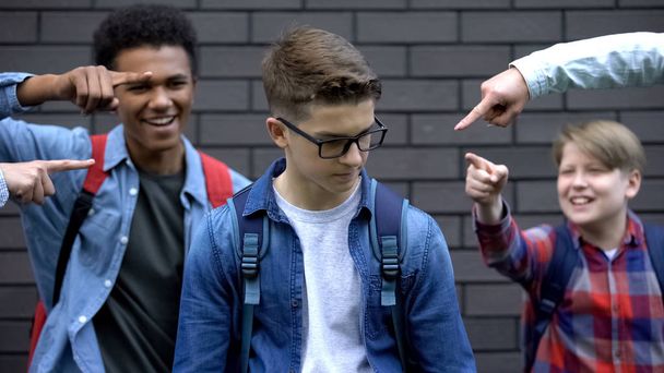 Cruel schoolchildren pointing fingers at student, mocking smart boy, bullying - Foto, afbeelding