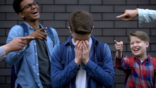 Cruel teenagers pointing at boy crying, emotionally depressed victim of bullying - Foto, afbeelding