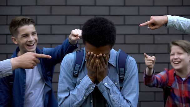 Mean teenagers pointing fingers at black boy crying, verbal bullying, bad rumors - Foto, afbeelding