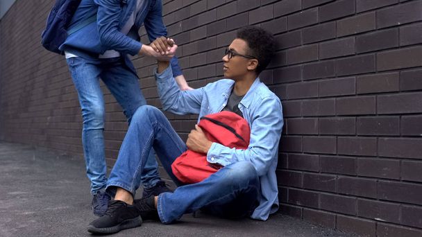 Teenage student giving helping hand to bullied afro-american boy, stop racism - Foto, afbeelding