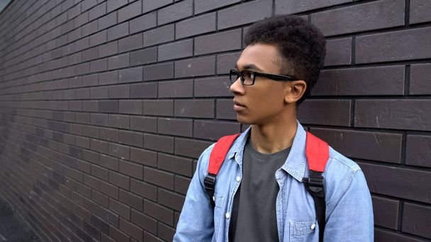 Scared black boy leaning against wall, intimidated victim of racial bullying - Фото, изображение