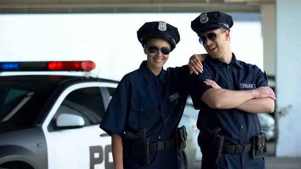 Vriendelijke politieagenten in uniform en glazen glimlachen om camera, wet en orde - Foto, afbeelding