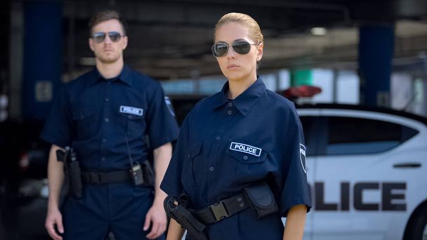 Vakava nainen ja mies poliisit aurinkolasit seisoo ulkona, turvallisuus
 - Valokuva, kuva