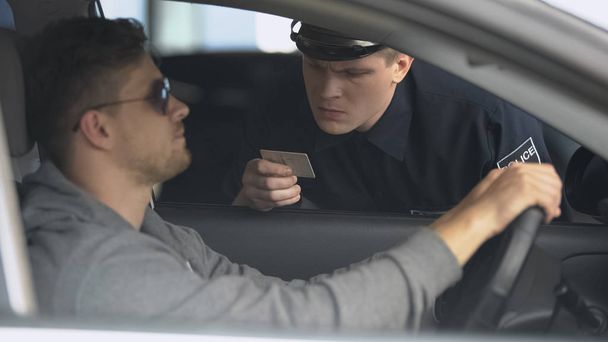 Serious policeman checking male drivers license after exceeding speed limit - Photo, image