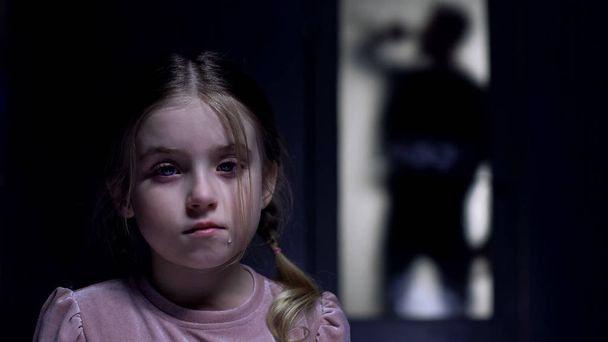 Crying little girl looking at camera silhouette of alcoholic father outside door - Фото, изображение