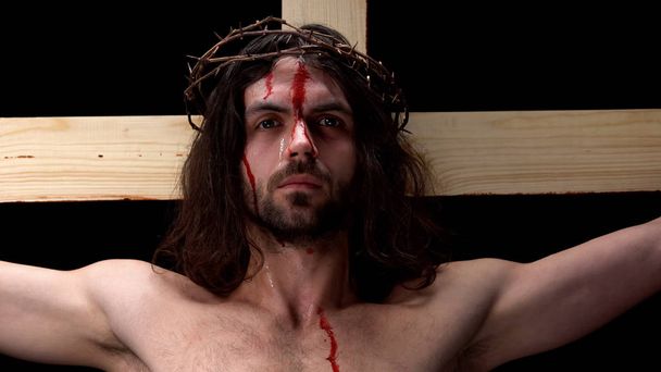 Crying son of God in thorns crown suffering on wooden cross, symbol of faith - Foto, imagen
