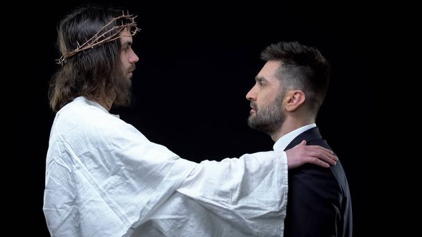 Forgiving Christ putting hand on businessman shoulder, looking each other, faith - 写真・画像