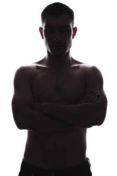 Silhouettenporträt eines jungen Mannes mit nacktem Oberkörper und verschränkten Armen. - Foto, Bild