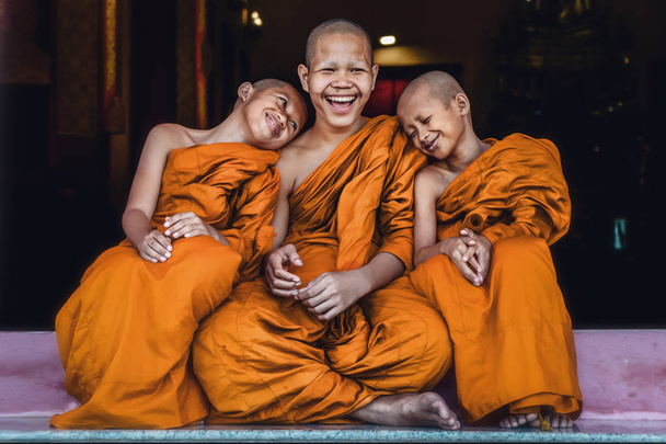 Three Thai Buddhist novices sitting together at temple door feeling happy and smile - 写真・画像