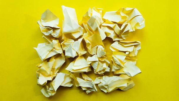 Ball crumpled paper ball isolated on a yellow background. Crumpled paper for texture. Crumpled paper after a brainstorming was thrown into the bin. A piece of yellow crumpled paper on a yellow backgro - Valokuva, kuva