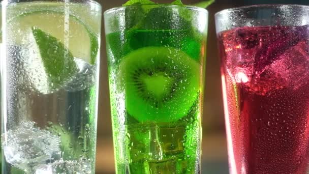 close-up de três cocktails com gelo. com uma folha de hortelã e um pedaço de kiwi. Cocktail vermelho com Basil. Água espumante transparente com fatias de vidro de limão
. - Filmagem, Vídeo