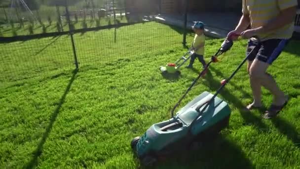 Cute little boy with gardener man mowing cutting grass lawn. Gimbal movement - Footage, Video