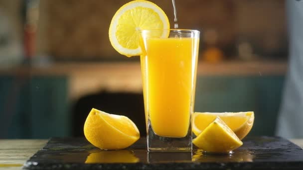 El hombre presiona jugo de naranja fresca en un vaso de vidrio en una bandeja negra contra el fondo de la cocina con los dedos. El agua gotea de la taza. Siguiente rebanadas de fruta es un montón de salpicaduras alrededor
. - Imágenes, Vídeo
