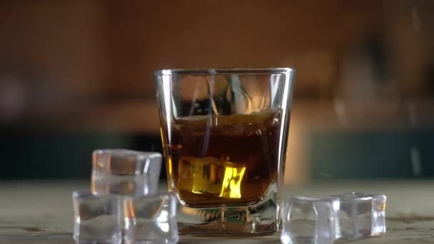 ijsblokjes vallen in een helder glas sterke single malt whisky wat een grote plons geeft. Het glas staat op een zwarte standaard. Ga naast de ijskristallen liggen. Feestelijke alcoholische drank voor kenners. - Video