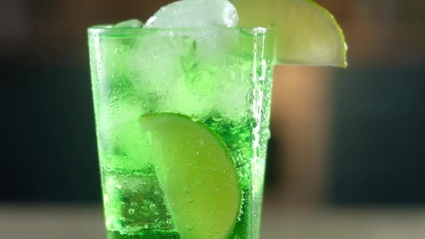 v mokré sklenici čiré sklo s kapkami vody nalil zelený koktejl s velkými kostkami studeného ledu. Na okraj sklenice byl položen plátek čerstvého vápna. Slavnostní nápoj na nový rok - Záběry, video