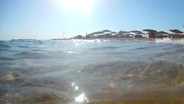 Ondas de luz surfar na praia de areia com guarda-sóis de praia de palha em um dia ensolarado claro, Mar Vermelho, vista de baixo, ângulo largo. Movimento lento Movimento padrão
 - Filmagem, Vídeo