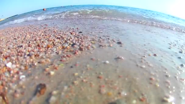 Leichte Wellen surfen auf dem Sandstrand mit reetgedeckten Sonnenschirmen an einem klaren, sonnigen Tag, rotes Meer, Blick von unten, Weitwinkel. Standardbewegung in Zeitlupe - Filmmaterial, Video