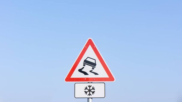 verkeersbord waarschuwt over gladde weg - Foto, afbeelding