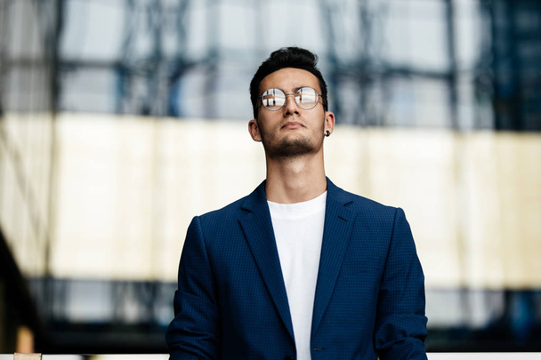 Architect in glasses dressed in stylish clothes stands on the background of a modern glass building - Фото, изображение