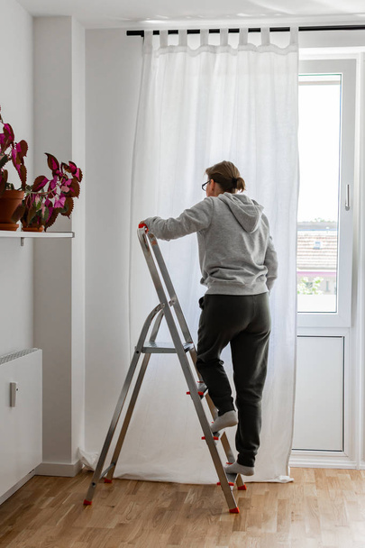 Женщина вешает белые занавески на стержень
 - Фото, изображение
