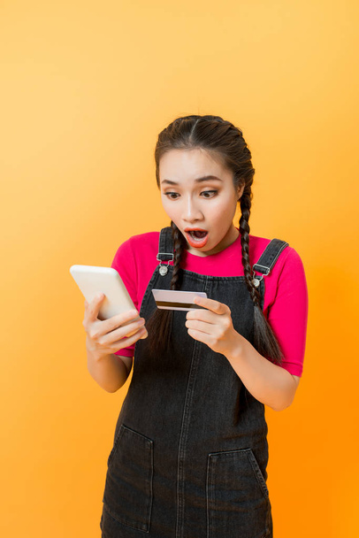Mujer asiática usa teléfono inteligente para pagar compras en línea con tarjeta de crédito en blanco, fondo amarillo
 - Foto, imagen