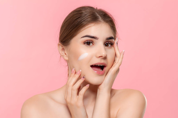 Beautiful model applyes moisturizing cosmetic product to skin holding white tube of a hyaluronic cream isolated over pink background. - Foto, Imagem