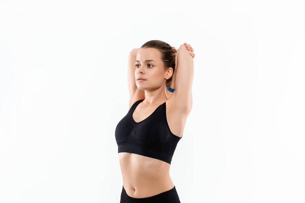 Young sporty blond woman in a black sportswear stretching before exercising isolated over white background. - Photo, Image