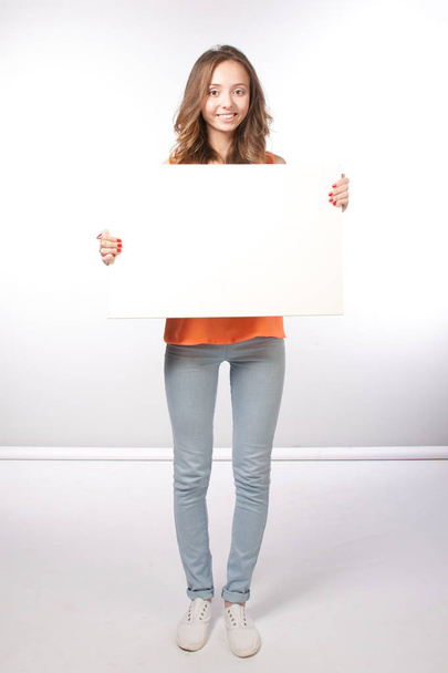 Cute smiling girl holding a blank white sheet on white backgroun - Photo, image