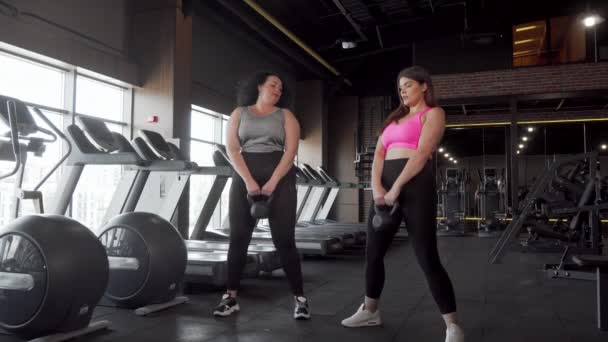 Dwa piękny plus rozmiar kobiet sportowców kucki z Kettlebells na siłowni - Materiał filmowy, wideo