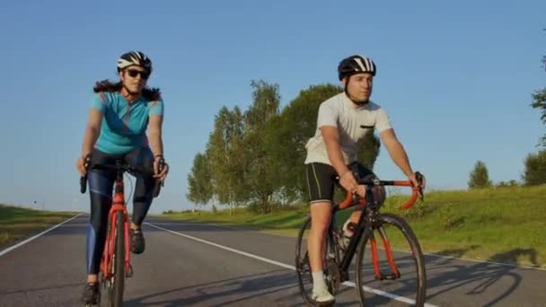 Kaksi ammattimaista maantiepyöräilijää ajaa pyörillään kukkulalla. Kädessä pidettävä laukaus kaksi vahvaa pyöräilijää naaras ja uros heidän koulutus lämmin mutta tuulinen kesäpäivä
. - Materiaali, video