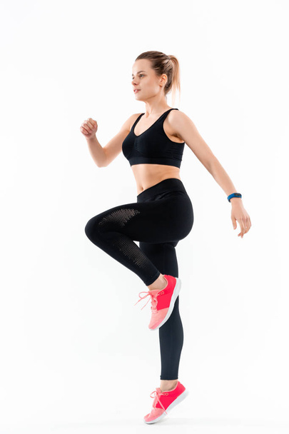Young sporty blond woman in a black sportswear jumping isolated over white background. - Foto, imagen