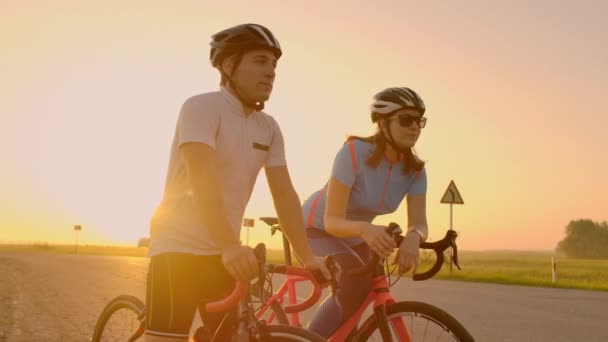 Un homme et une femme en casque avec des vélos se tiennent debout et parlent au coucher du soleil. Reposez-vous après une balade à vélo sur l'autoroute. Piste de vélos. Sport en couple
. - Séquence, vidéo