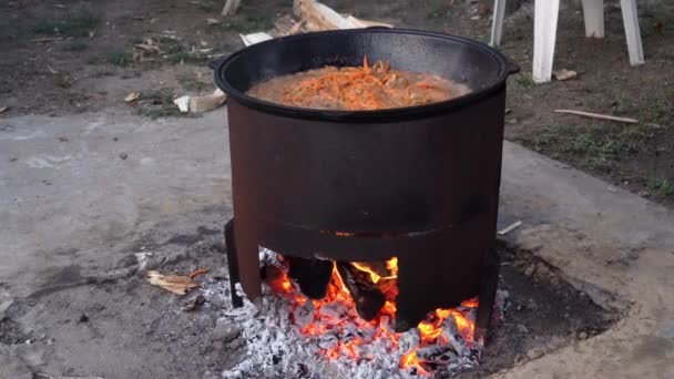Cooking pilaf in a large pot over an open fire. Fry meat, onions, carrots. Delicious rice. Street kitchen. - Záběry, video