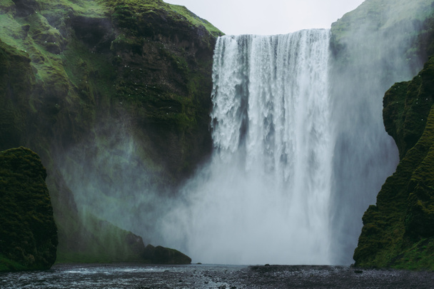 Majestuosa cascada Skogarfoss en Islandia. Salpicaduras blancas y verdes volando contra verdes colinas cubiertas de musgo
. - Foto, Imagen